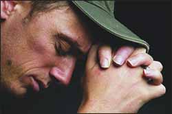 White man in baseball cap praying, left